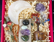 Aquarius zodiac crystals. A collection of tumbled crystals including Amethyst, Aquamarine, and Labradorite, with a crystals sticker card, dried flowers, a moon, heart-shaped selenite bowl, and a 6mm bracelet, all packaged in a gift box.